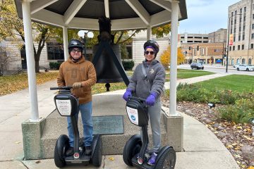 Couple in front of bell on Segways